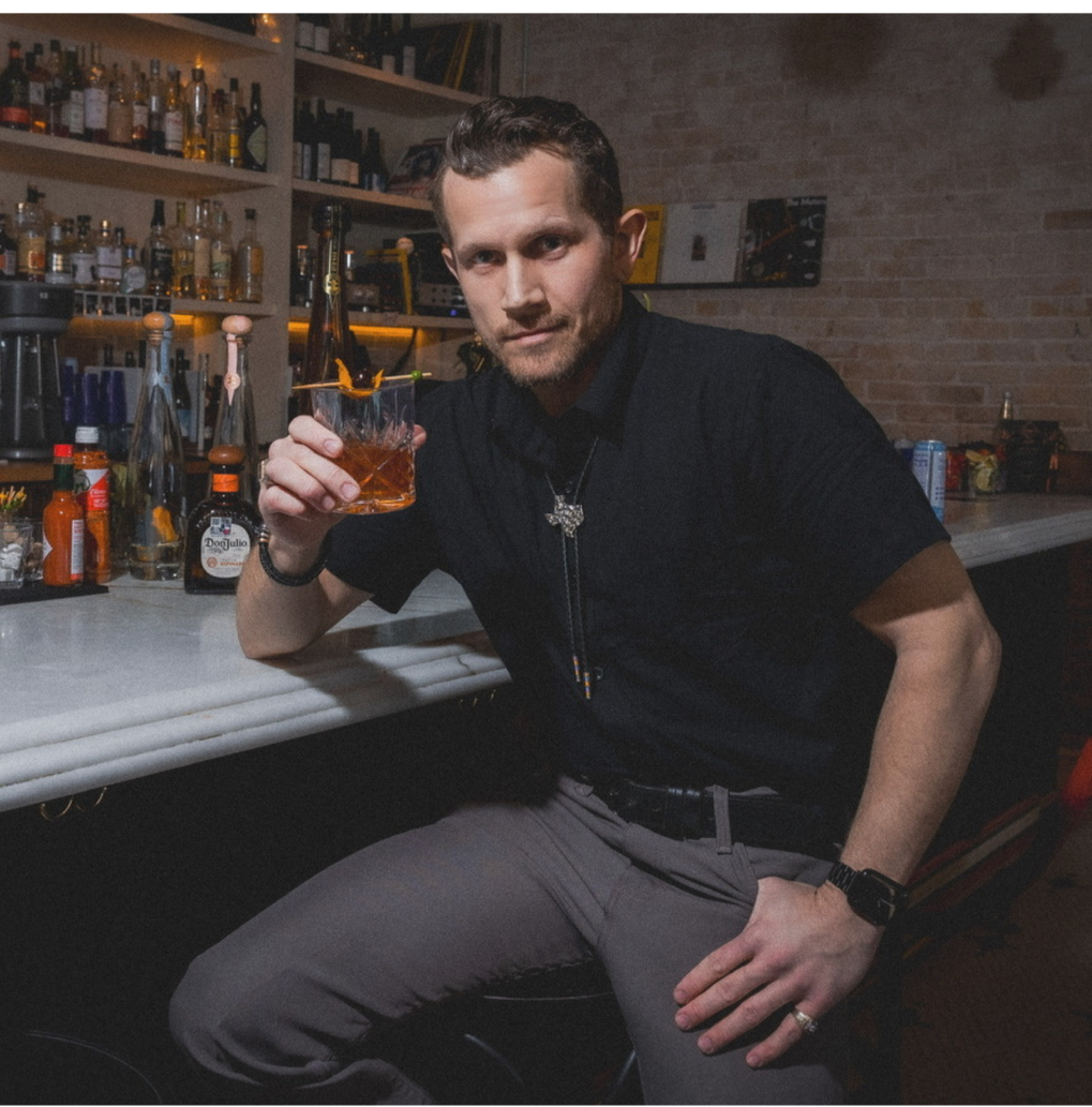 Black Orchid Bar Co. Founder Portrait — Austin Private Bartending Portrait of Sean Cope, founder of Black Orchid Bar Co., seated at a bar with craft spirits and glassware in the background.